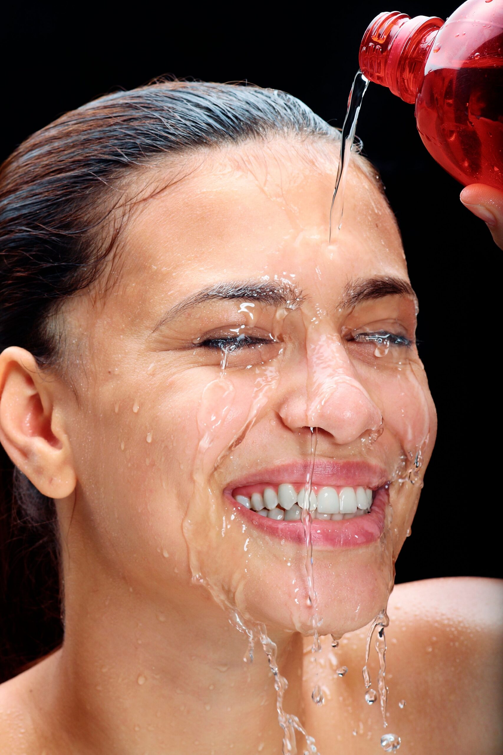 Close-up of a smiling woman pouring water over her head in a refreshing, joyful moment.